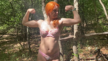 Sexy redhead Strong woman showing her big muscles in the forest, Face included in the video